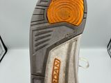 la semelle d'une paire de chaussures blanches à semelles orange posée sur une surface blanche
