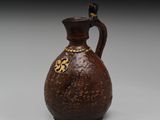 un vieux vase marron orné d'un motif doré sur l'anse