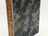 an old book sitting on top of a white surface covered in clouds