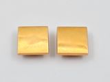 une paire de boucles d'oreilles carrées en or posées sur une surface blanche