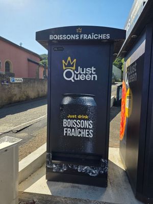 une affiche sur le bord de la route sur laquelle on peut lire « Just Queen, Just Drink Boissons Fraîches »