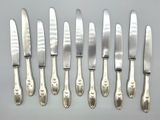 six silverplated knives and six knives on a white surface