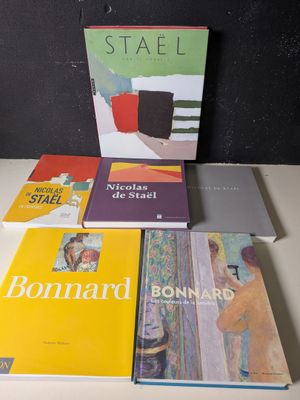 Plusieurs livres sont empilés sur une table devant un mur noir.