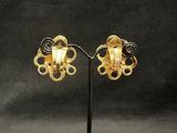 a pair of gold earrings on a stand against a black background