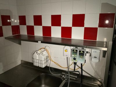 un évier dans une petite cuisine dont les murs sont carrelés de rouge et de blanc