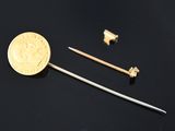 une pièce d'or et une petite épingle en métal posées sur une surface noire