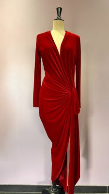 La robe est rouge, elle a des manches longues et un drapé sur le côté.