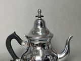 a silver tea pot with a black handle on a table