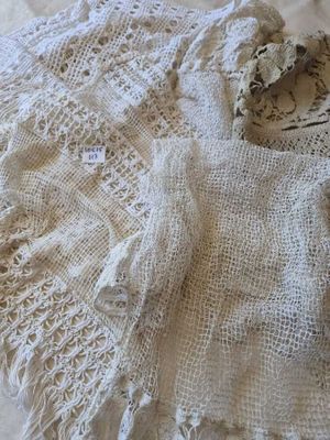 un pull blanc au crochet posé sur un lit, à côté d'une paire de chaussures