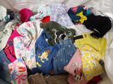 a pile of clothes on a bed with a teddy bear