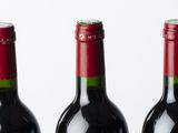 four bottles of red wine lined up in a row on a white surface