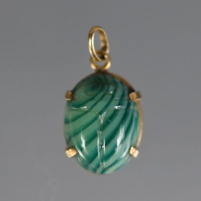 une photo d'un pendentif vert et doré sur fond blanc