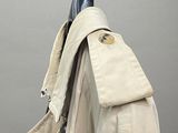 beige trench coat hanging on a hanger against a gray wall