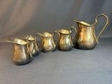 four silver pitchers and a pitcher are lined up on a gray background