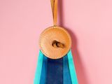 a blue and green ribbon with a wooden button on a pink background