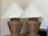 pair of wicker lamps with white shades on top of a table