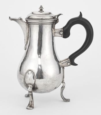 an antique silver coffee pot with a black handle on a stand