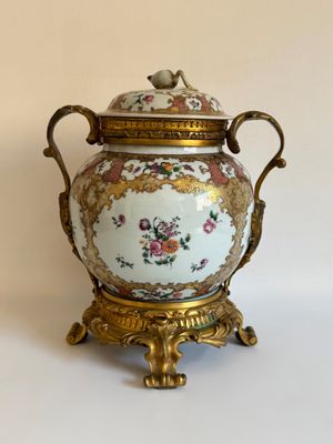 un vase blanc et doré muni d'un couvercle, posé sur un socle