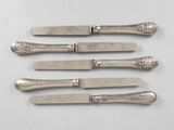 six silverplated knives with ornate designs on them on a white surface