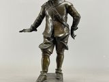 statue en bronze représentant un homme coiffé d'un chapeau, posée sur un socle en bois