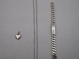 a silver bracelet and a silver heart charm on a table