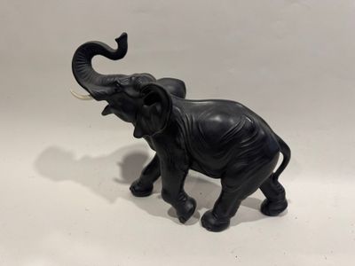 un petit éléphant noir debout sur une surface blanche