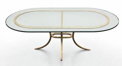 une table à manger ovale en verre avec des pieds en métal doré et un plateau en verre