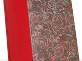 un vieux livre à la couverture rouge posé sur une table blanche