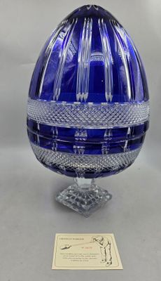 une photo représentant un œuf en verre bleu posé sur un socle, accompagné d'une carte