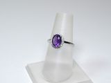 une image représentant une bague ornée d'une pierre violette posée sur un socle blanc