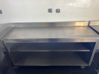 une table en acier inoxydable dans une cuisine au sol carrelé de noir