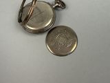 a silver pocket watch and a coin on a white surface