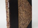 an old book with a black cover and gold trim on a white background