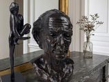 a statue of a man sitting on a table next to a vase of flowers