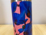 thermos cup on a wooden table with a pink background and blue flowers