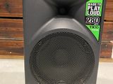 un gros plan sur une enceinte posée au sol, avec une boîte en arrière-plan