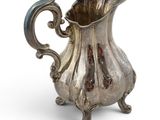 an antique silver pitcher on a stand on a white background