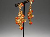 a pair of gold and coral earrings on a black stand