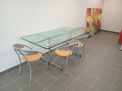 une table et des chaises en verre dans une pièce où est accroché un tableau au mur