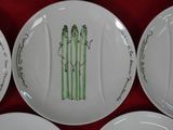 four white plates with green asparagus designs on them on a red cloth