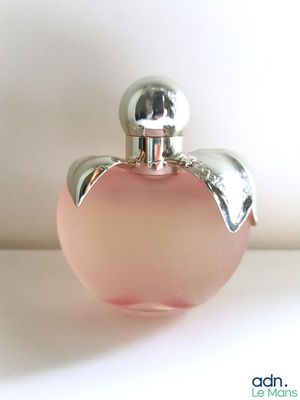 un flacon de parfum en verre rose avec un bouchon argenté, posé sur une surface blanche