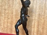 une statue antique en bronze représentant un homme tenant une raquette de tennis