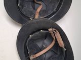 two black hats with leather straps are sitting on a white surface