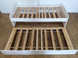 a white bed frame with wooden slats on the floor