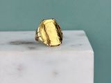 La bague en or repose sur un bloc de marbre blanc.