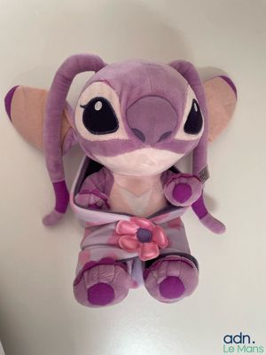 purple stuffed animal sitting on a white surface with a pink bow