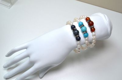 une main de mannequin blanche tenant un bracelet orné de perles multicolores