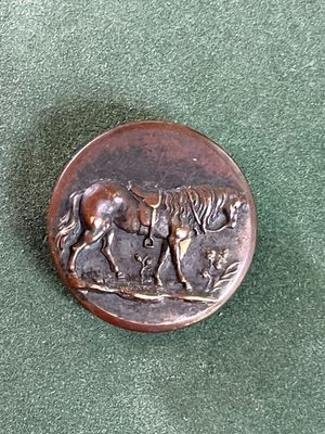 un bouton en métal représentant un cheval sur un fond vert