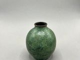 un petit vase vert posé sur une surface blanche