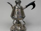 an antique silver teapot with a black handle on a stand